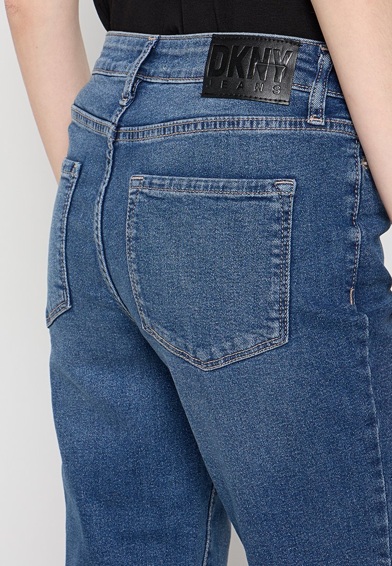 Jeans in denim blu con vita alta, caratterizzati da un'etichetta con il logo DKNY sul retro, design a cinque tasche e dettagli di cucitura sottili.
