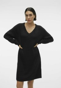 Abito in maglia oversize nero con scollo a V, maniche lunghe e orlo a costine. Tessuto morbido, lunghezza al ginocchio, vestibilità comoda senza motivi né decorazioni.
