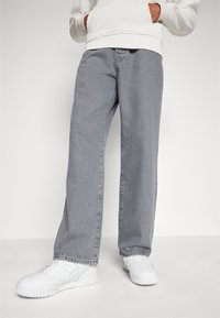 Light gray denim jeans with a straight-leg fit, featuring front pockets, a zip fly, and frayed hems, paired with white sneakers.