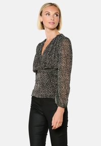 Blusa leopardata nera e beige con maniche lunghe e trasparenti e scollatura a V, caratterizzata da un punto vita arricciato per un silouette aderente.