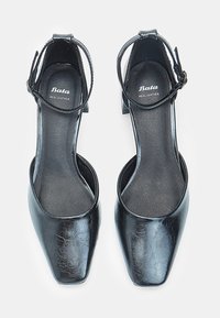 Black leather heels with a square toe, ankle strap, and a low block heel. Interior features smooth leather lining. Brand label visible.