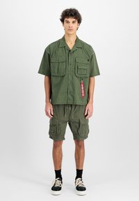 Camicetta a maniche corte verde oliva con due tasche sul petto, abbinata a pantaloni cargo coordinati con più tasche e una vita regolabile.