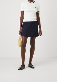 Bílý žebrovaný top s krátkým rukávem a černým lemem, doplněný tmavě modrou sukní áčkového střihu. Černé baleríny a malá žlutá prošívaná kabelka dokončují vzhled.