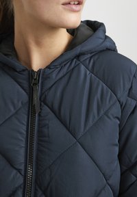 Marineblaue gesteppte Jacke mit Kapuze, Reißverschluss und glatter Textur. Auffälliges Rautenmuster und kontrastierendes Innenfutter.