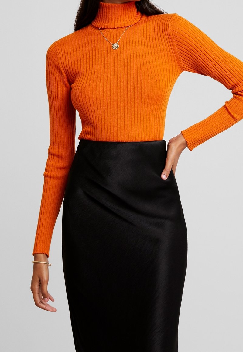 Oranžový žebrovaný rolák spárovaný s elegantní černou saténovou sukní, která zdůrazňuje obepínající střih a hladké textury.