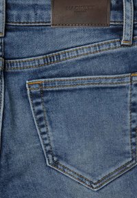 Jeans de denim con un lavado azul claro, sutil textura y costuras amarillas contrastantes. Etiqueta de cuero con la inscripción "HACKETT LONDON" sobre el bolsillo trasero.