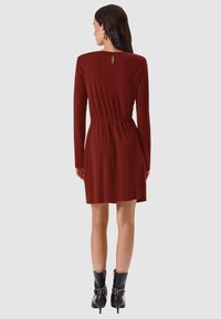 Abito a maniche lunghe color ruggine con vita aderente e dettaglio a goccia sulla schiena. Abbinato a stivaletti neri con borchie decorative.