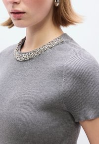 Γκρι ριμπ πλεκτό τοπ με λαμπερό λαιμόκοψη από χάντρες  και κοντά μανίκια, που αναδεικνύει την υφή και τη λεπτομέρεια στο σχέδιο.