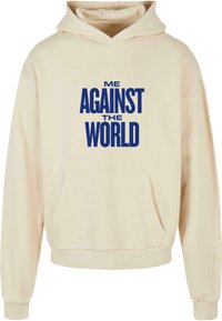 Felpa beige con tasca frontale, caratterizzata da un audace testo blu che recita "ME AGAINST THE WORLD" sul petto. Tessuto pesante, vestibilità rilassata.
