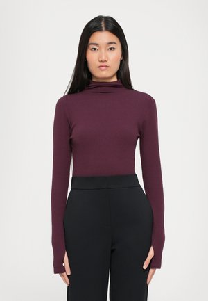Langarm-Turtleneck-Oberteil aus tiefburgunderfarbigem Stoff. Glatte Textur, taillierte Passform, kombiniert mit hochgeschnittenen schwarzen Hosen. Minimalistischer Stil.