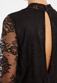 Zwarte kanten jurk met lange mouwen met een bloemenpatroon en een keyhole achterkant, vastgemaakt met twee knopen. Zacht, gestructureerd materiaal.