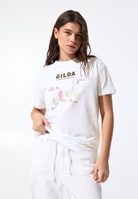 T-shirt en coton blanc avec impression graphique d'un piment, d'une olive et d'une anchois avec le texte "GILDA" en dessus. Manches courtes, coupe décontractée.