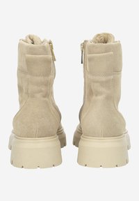 Beige Wildleder-Stiefeletten mit glatter Textur, ausgestattet mit einem gepolsterten Kragen und einem seitlichen Reißverschluss, auf einer klobigen beigen Sohle.