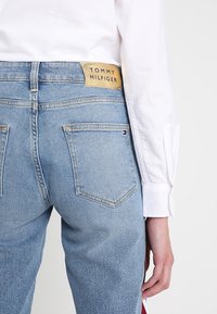 Jasnoniebieskie dżinsy z wysokim stanem, z beżową metką Tommy Hilfiger z tyłu i dwiema standardowymi kieszeniami z tyłu.