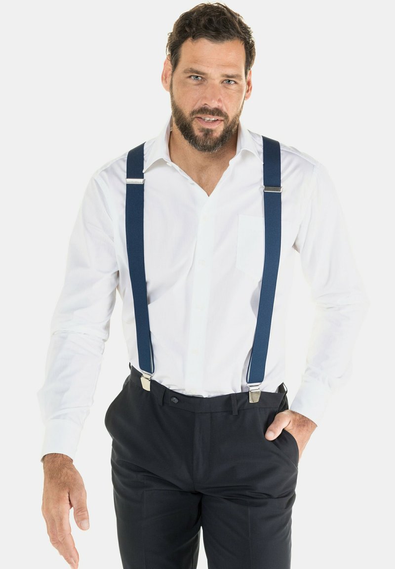 Tirantes azul marino con clips plateados llevados sobre una camisa blanca de botonadura, combinados con pantalones oscuros. Tejido suave con un diseño clásico.