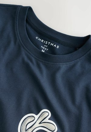 Tums zilā kokvilnas t-krekls ar apaļu kaklu; priekšpusē ir baltā krāsā stilizēta burtiņu grafika.