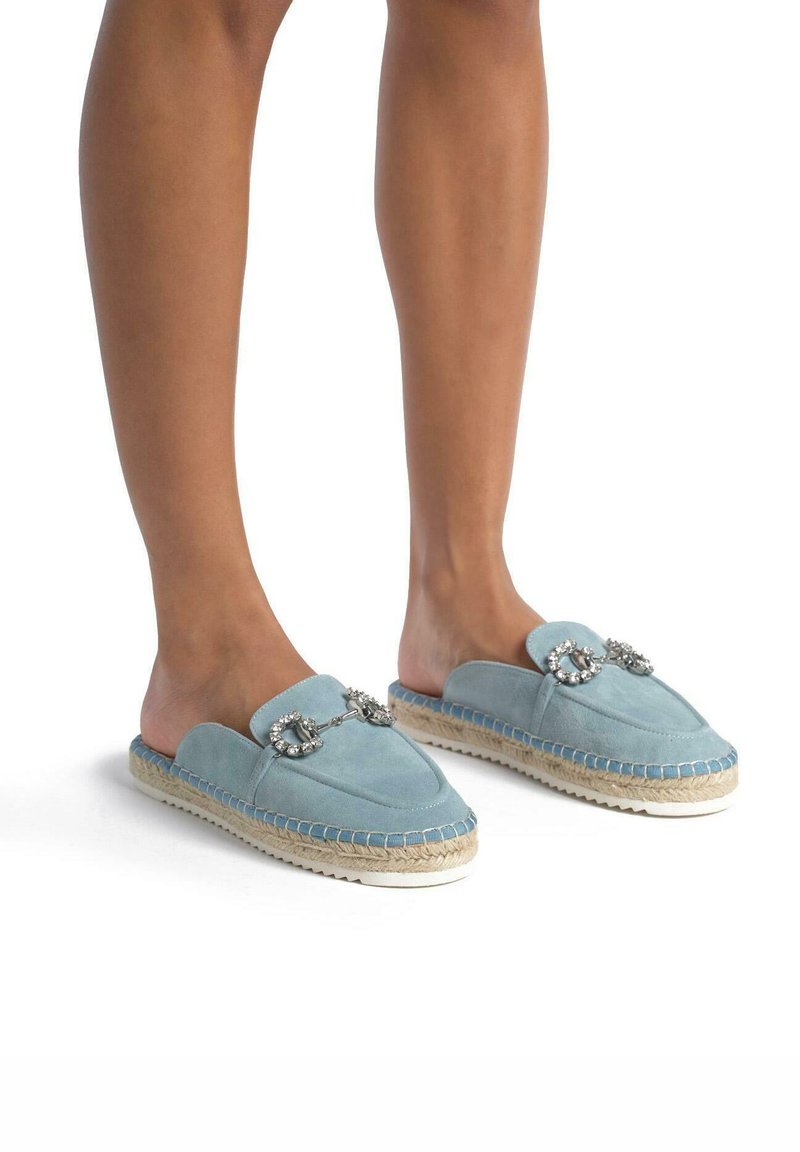 Scarpe slip-on in suede blu con una texture morbida, caratterizzate da dettagli gioiello e suole in juta intrecciata. Design con punta arrotondata e retro aperto.