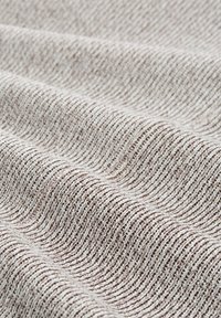 Close-up van beige en bruin gebreide stof met zichtbare geribbelde textuur en zachte geplooide golven.