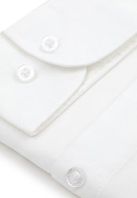 Biała tkanina o gładkiej fakturze, z dwoma przezroczystymi guzikami z wygrawerowaną nazwą marki oraz z złożonym detalem klapki.