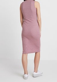 Robe sans manches, ajustée, arrivant au genou dans une couleur rose chiné, fabriquée en tissu extensible, associée à des baskets blanches.