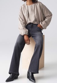 Cazadora bomber beige con puños elásticos, combinada con vaqueros acampanados gris oscuro y botines negros puntiagudos. Tejido texturizado, corte relajado.