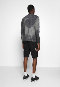 T-shirt à manches longues gris tie-dye avec le texte blanc "AMERICAN EAGLE" sur la manche, associé à un short cargo noir et des baskets noires.