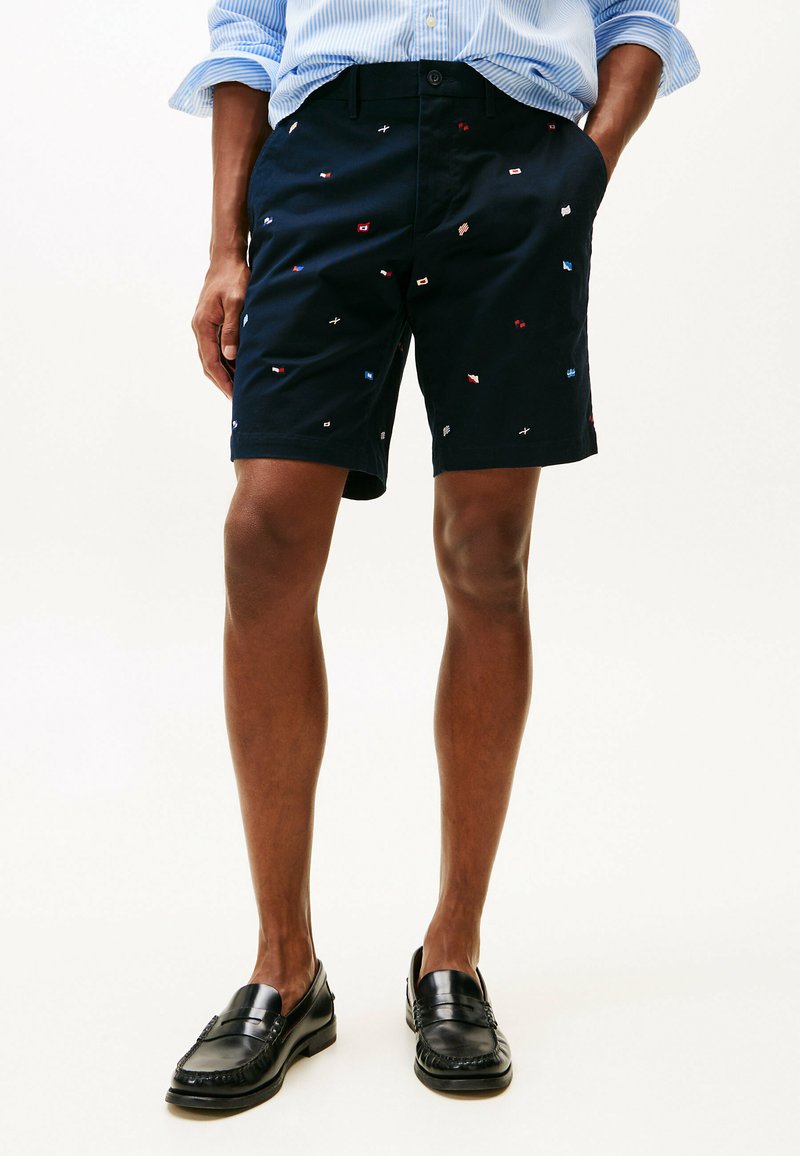 Pantaloni corti navy con motivi di bandiera ricamati multicolori, caratterizzati da una vestibilità dritta, tasche laterali e chiusura frontale con bottone.