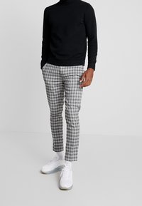 Suéter negro ajustado de cuello alto, pantalones de cuadro gris y blanco con corte slim, combinados con zapatillas deportivas blancas y calcetines blancos.