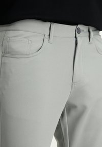 Pantaloni grigi chiari con una texture, dal design aderente, dotati di una chiusura con zip, bottone e una tasca laterale.