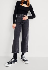 Svart ribbat långärmad topp med utskärningsdesign, parat med grå högmidjade vida jeans och svarta sneakers med vita detaljer.