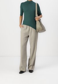 Green ribbed short-sleeve top, beige loose-fitting trousers, and black flat shoes. Model holds a gray shoulder bag. Simple and modern design.