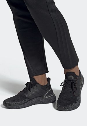 Des chaussures de sport noires avec une tige en maille texturée, un support de talon moulé et une semelle en caoutchouc à motifs. Associées à un pantalon noir fuselé.