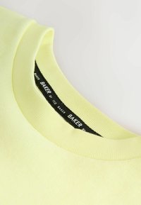 Żółta bawełniana koszulka z okrągłym dekoltem i ribbowym wykończeniem, z czarną metką wewnątrz kołnierza z napisem "BAKER by TED BAKER".