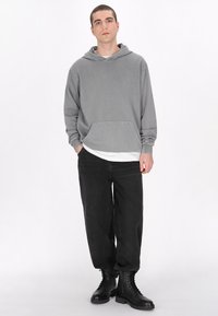 Szürke kapucnis pulóver, zsebbel, egy fehér póló fölött viselve. Fekete, laza szabású farmernadrág és fekete fűzős bakancs egészíti ki az öltözetet.