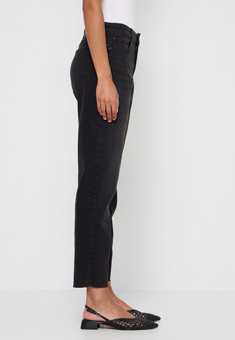 Schwarze Denim-Jeans mit geradem Schnitt, hoher Taille und subtilen Stickdetails. Getragen mit schwarzen, gewebten Slippern.