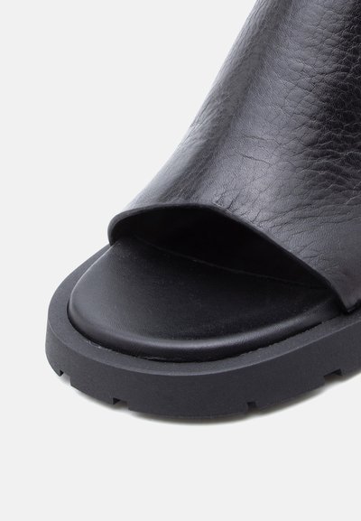 Μαύρο δερμάτινο σανδάλι ανοιχτής μύτης με χοντρή υφασμάτινη σόλα και φαρδιά λωρίδα που καλύπτει το πάνω μέρος του ποδιού.