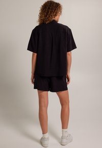 Černé tričko s krátkým rukávem a odpovídající šortky vyrobené z lehkého materiálu. Má uvolněný střih s límečkem a viditelnými detailem šití.