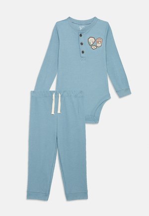 Blaues Waffelmuster-Zweiteiler-Outfit bestehend aus einem Langarm-Body mit drei Knöpfen und dekorativen Aufnähern, kombiniert mit passenden Hosen.