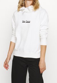 Sudadera blanca con capucha ajustable, que presenta un logo negro de "Lee Jeans" en el pecho. Puños y dobladillo acanalados, textura suave.