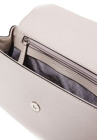 Jasnobeżowa torebka o teksturowanej powierzchni, z zamykaną na zamek kieszenią i wzorzystą podszewką. Widoczny detal z zatrzaskiem magnetycznym.