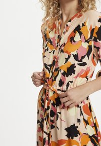 Bloemenpatroon jurk in pastelkleuren van perzik, oranje en zwart. Heeft korte mouwen, knopen en een verstelbare strik in de taille.