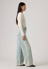 Φαρδιά τζιν παντελόνια σε ανοιχτό μπλε με ξεθωριασμένο πλύσιμο και ψηλή μέση, σε συνδυασμό με εφαρμοστή μακρυμάνικη μπλούζα σε εκρού χρώμα. Ορατές απλές ραφές.
