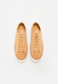 Tan mocka sneakers med snörning, vit gummisula och silverfärgade öglor. Har en slät yta och rund tå.