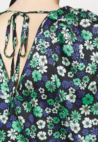 Bluzka w kwiatowy wzór na czarnym tle, z zielonymi i niebieskimi kwiatami, zawiązywana z tyłu, o luźnym, swobodnym kroju.