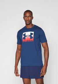 Mørkeblå bomulds t-shirt med et frontlogo, der har et gradient design i rød og hvid. Korte ærmer og rund hals.