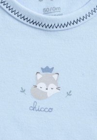 Vêtement bébé bleu clair avec couture en zigzag au niveau du col, ornée d'un petit visage de renard portant une couronne bleue et de feuilles décoratives vertes.