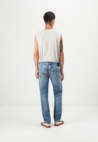 Light gray sleeveless shirt, blue faded jeans, and white sneakers with black accents, viewed from the back against a plain background.