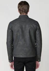 Giacca da uomo grigia scura in ecopelle con una texture liscia, tasche laterali con zip, colletto a scatto e dettagli imbottiti sulle spalle.