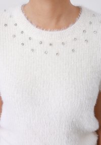 Pull blanc en maille présentant une finition douce et texturée avec des ornements en cristal ronds près de l'encolure et un ourlet inférieur côtelé.