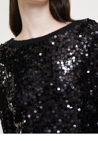 Svart pailletttröja med rund halsringning. Ytan är tätt täckt av glänsande svarta och silvriga cirkulära paljetter.